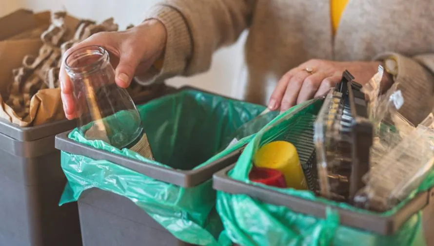 Manos de persona separando residuos plásticos en botes de basura